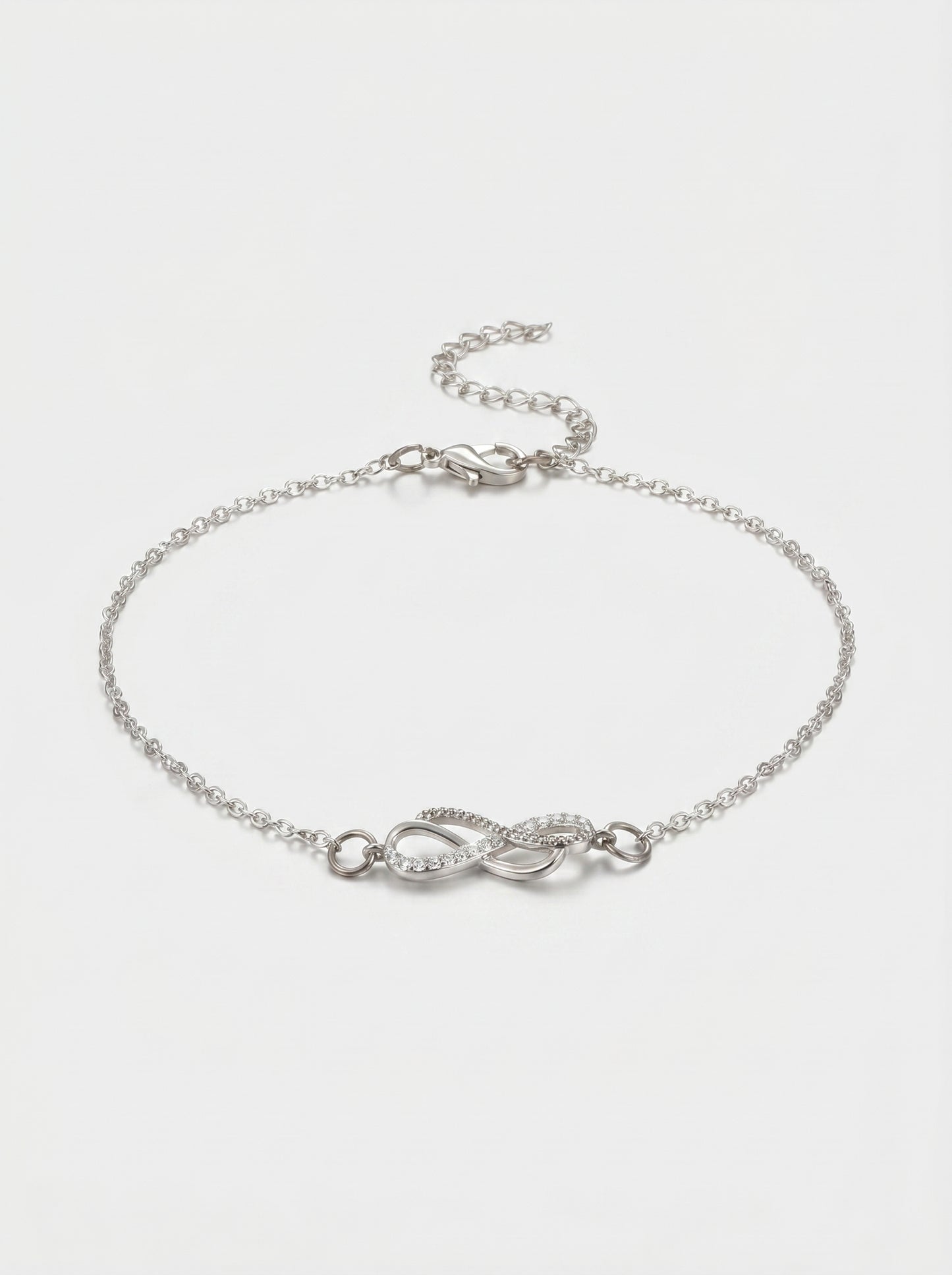 Pulseira prateada delicada com símbolo infinito, detalhe em cristais, corrente fina e fecho ajustável, fotografada sobre fundo claro para um visual elegante, feminino e minimalista.