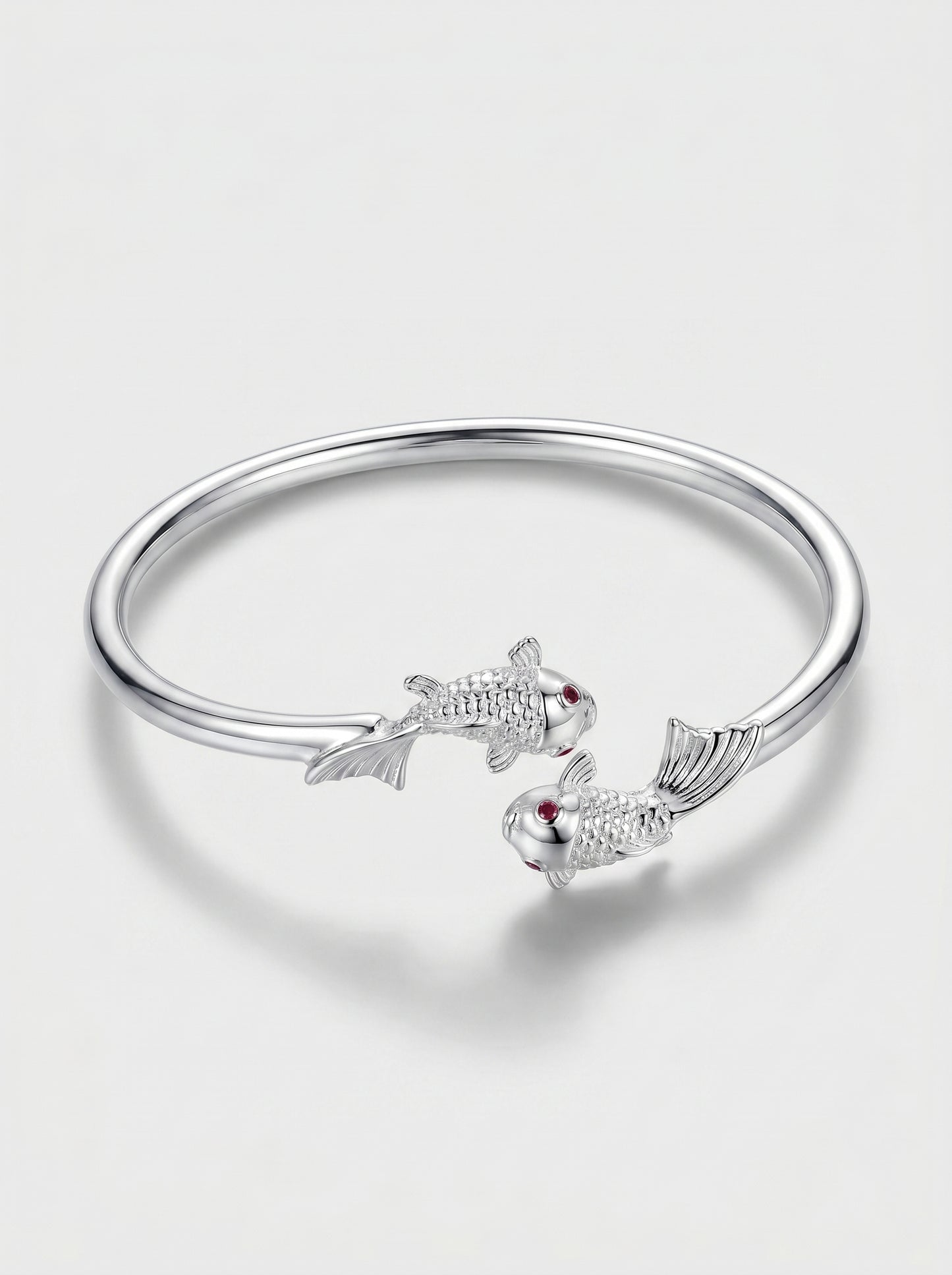 Pulseira prateada rígida com design aberto e detalhes delicados de peixes, fotografada sobre fundo claro para um visual elegante e minimalista.