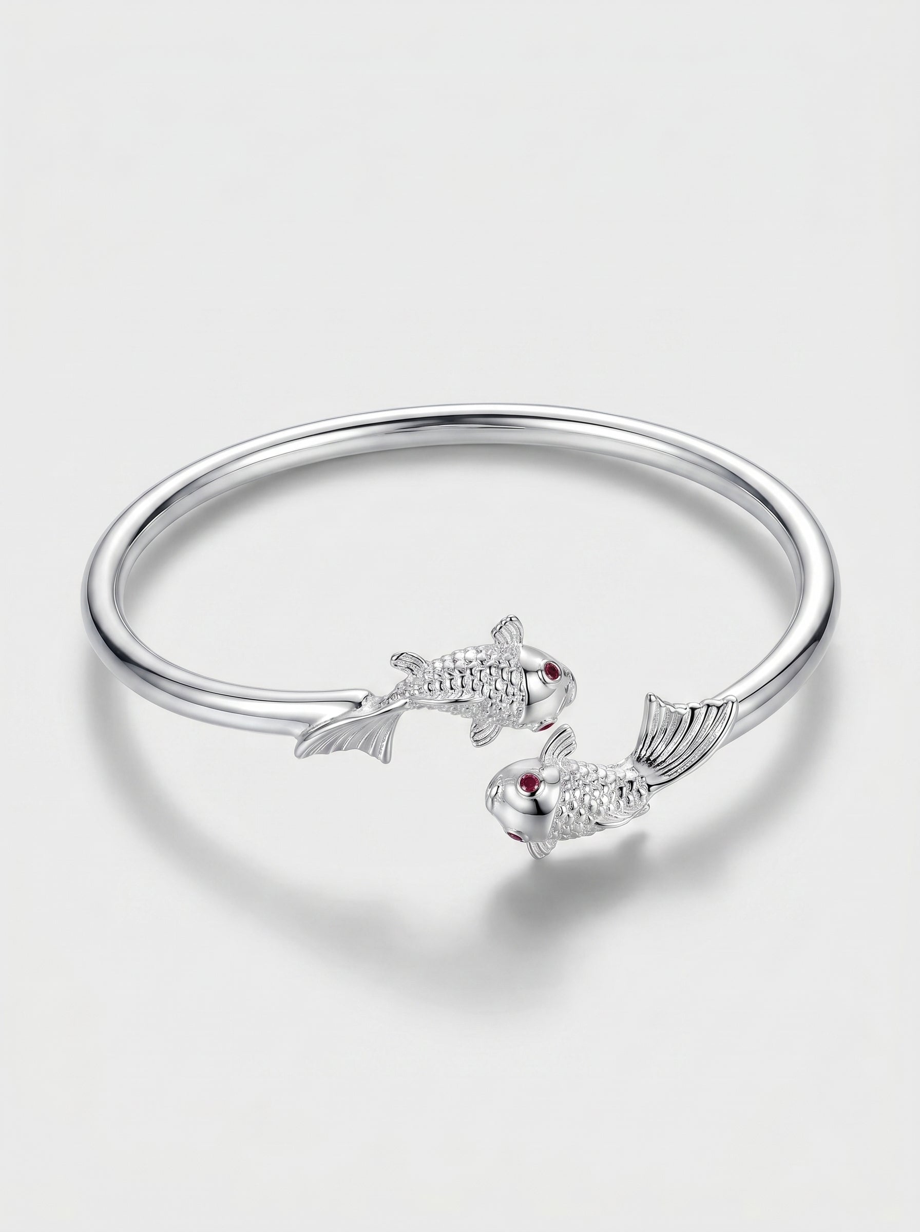 Pulseira prateada rígida com design aberto e detalhes delicados de peixes, fotografada sobre fundo claro para um visual elegante e minimalista.