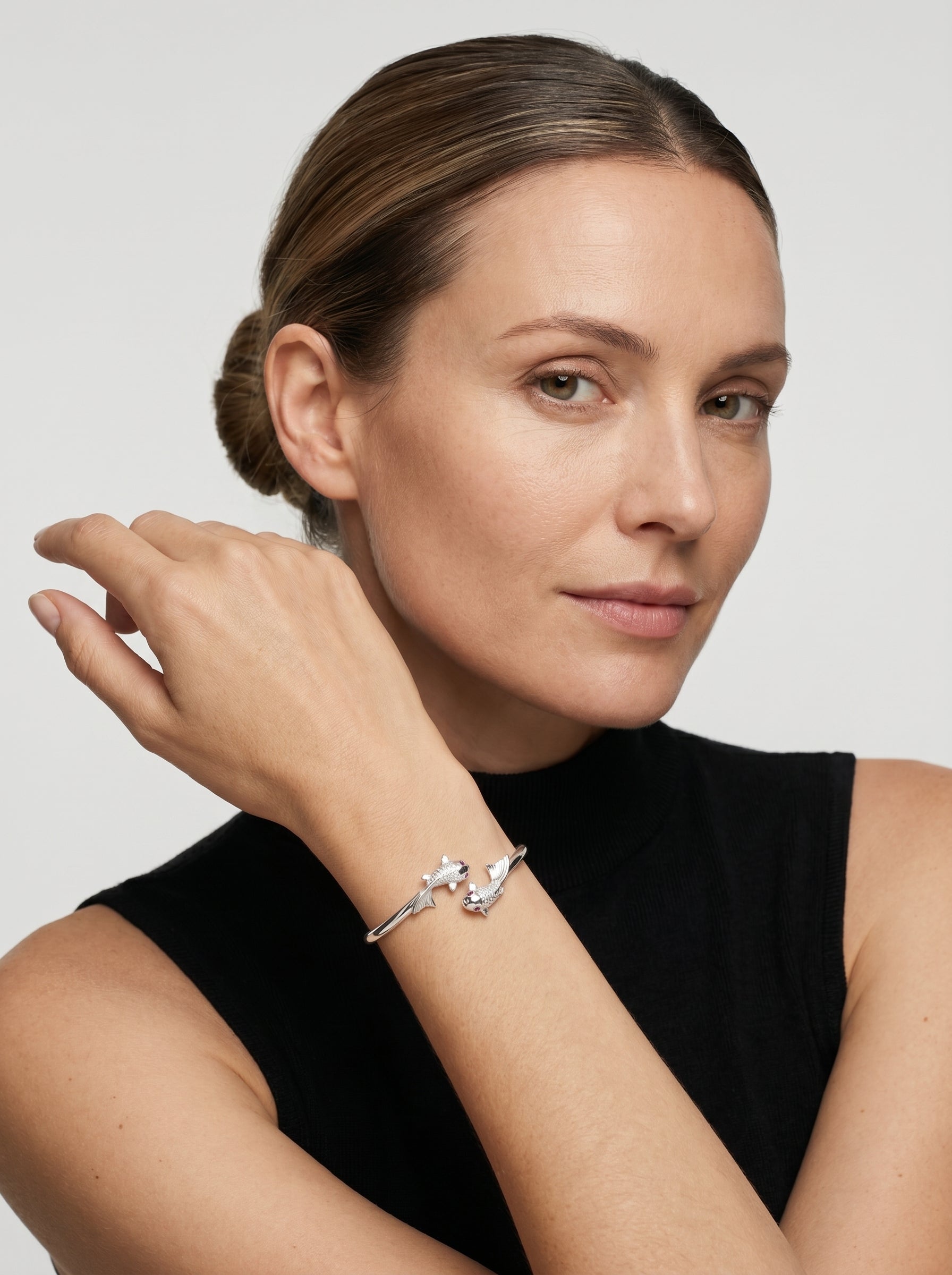 Pulseira prateada rígida com design aberto e detalhes delicados de peixes, usada por uma modelo para um visual elegante e minimalista.