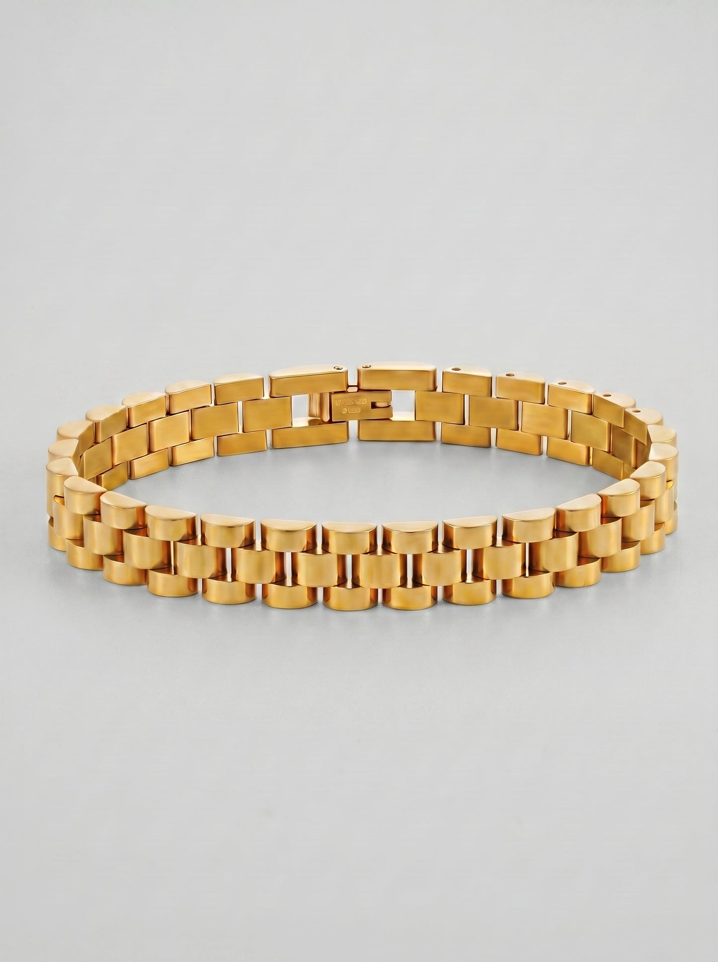 Pulseira dourada com design de elos largos e acabamento polido, fotografada sobre fundo cinzento claro para um visual elegante e sofisticado.
