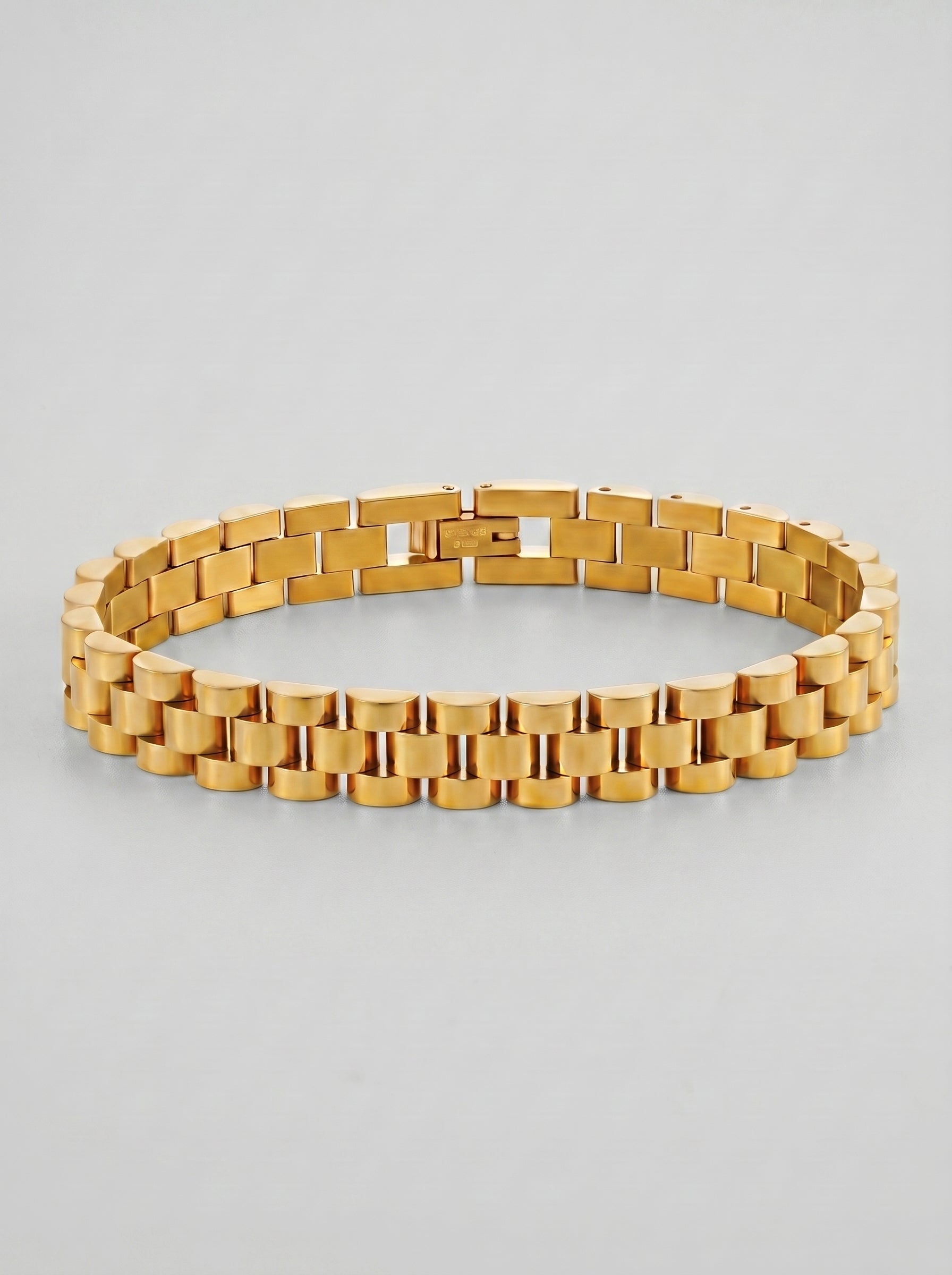 Pulseira dourada com design de elos largos e acabamento polido, fotografada sobre fundo cinzento claro para um visual elegante e sofisticado.