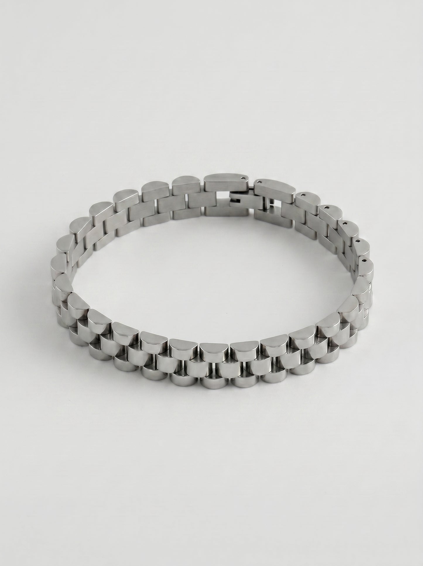 Pulseira prateada com design de elos largos e acabamento polido, fotografada sobre fundo cinzento claro para um visual elegante e sofisticado.