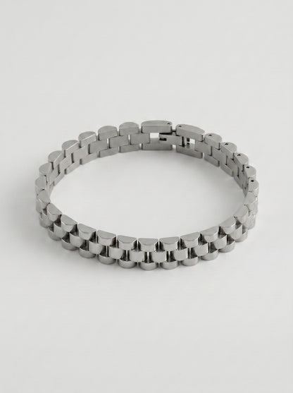Pulseira prateada com design de elos largos e acabamento polido, fotografada sobre fundo cinzento claro para um visual elegante e sofisticado.