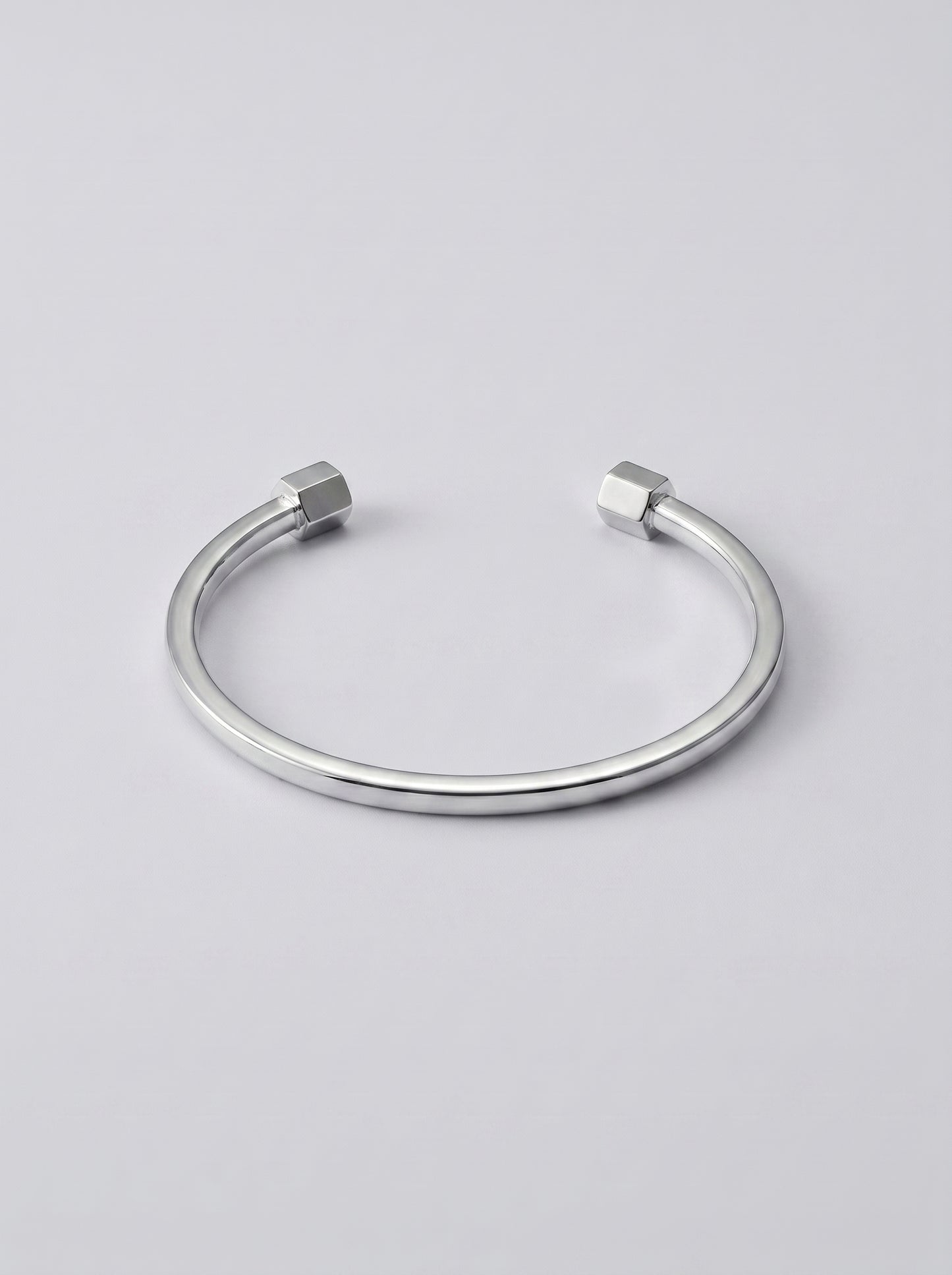 Pulseira prateada aberta com extremidades em forma de hexagono sobre fundo cinzento claro.