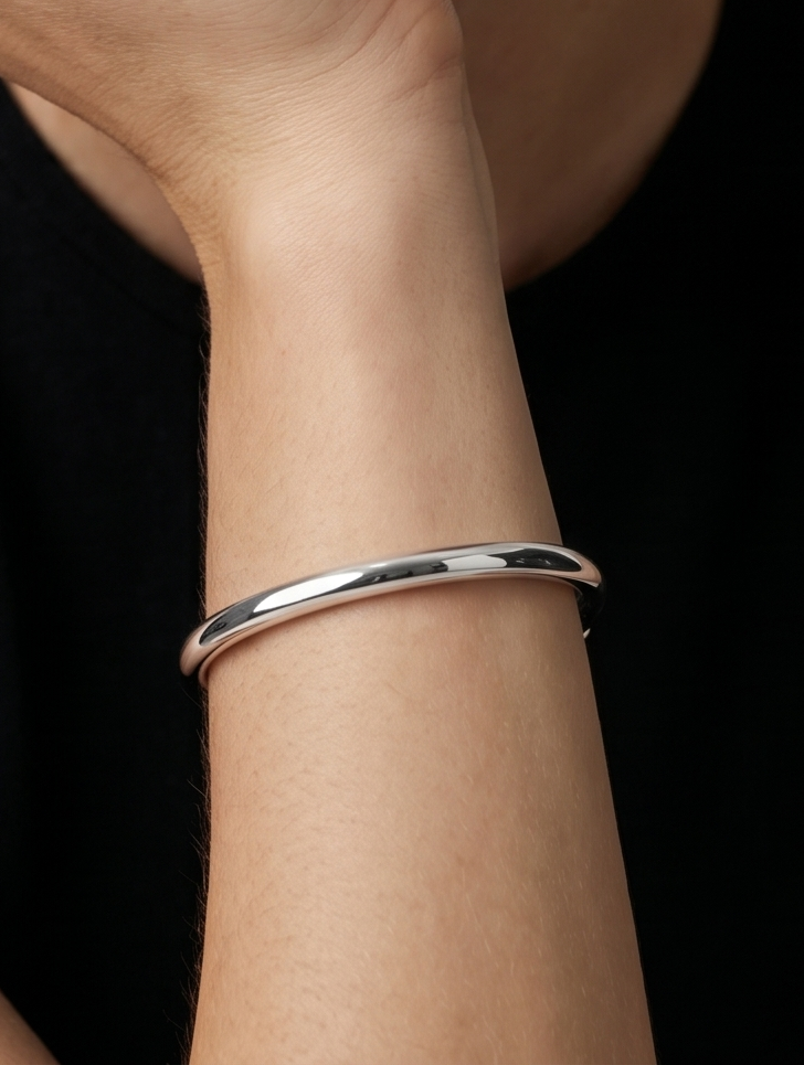 Pulseira prateada rígida com design aberto, acabamento polido e extremidades hexagonais, usada no pulso para um visual minimalista e moderno.