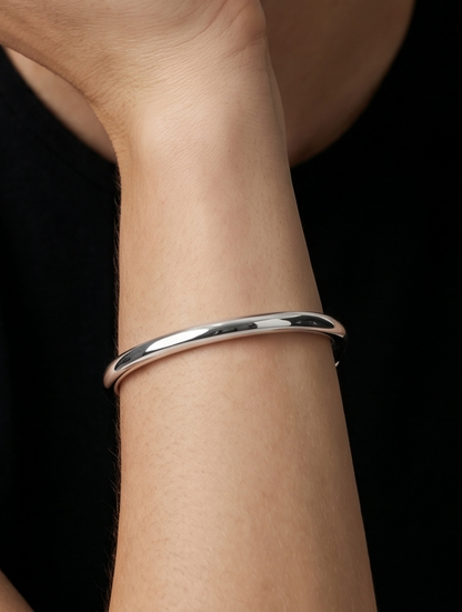 Pulseira prateada rígida com design aberto, acabamento polido e extremidades hexagonais, usada no pulso para um visual minimalista e moderno.
