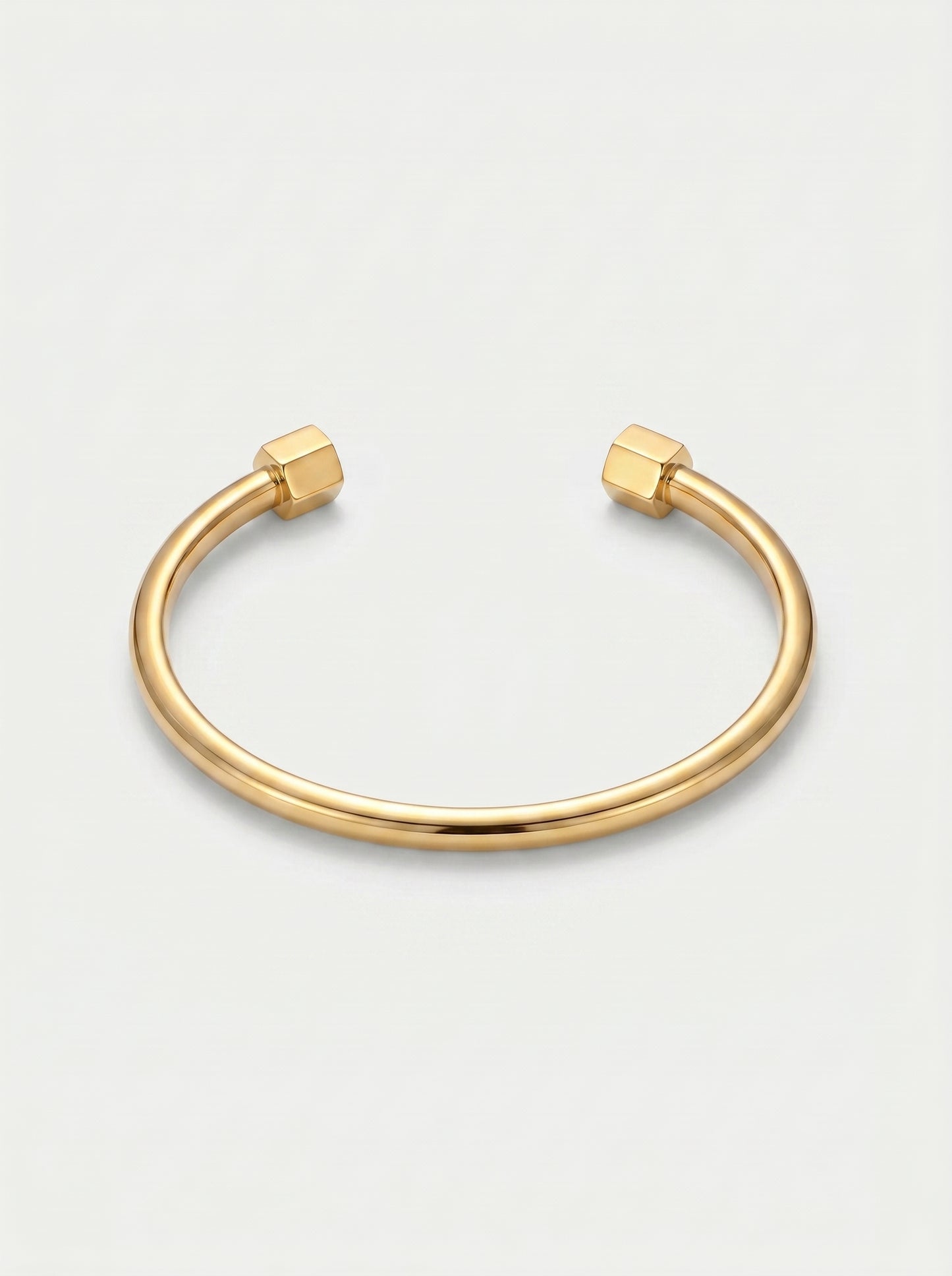 Pulseira dourada rígida com design aberto, acabamento polido e extremidades hexagonais, fotografada sobre fundo claro para um visual minimalista e moderno.