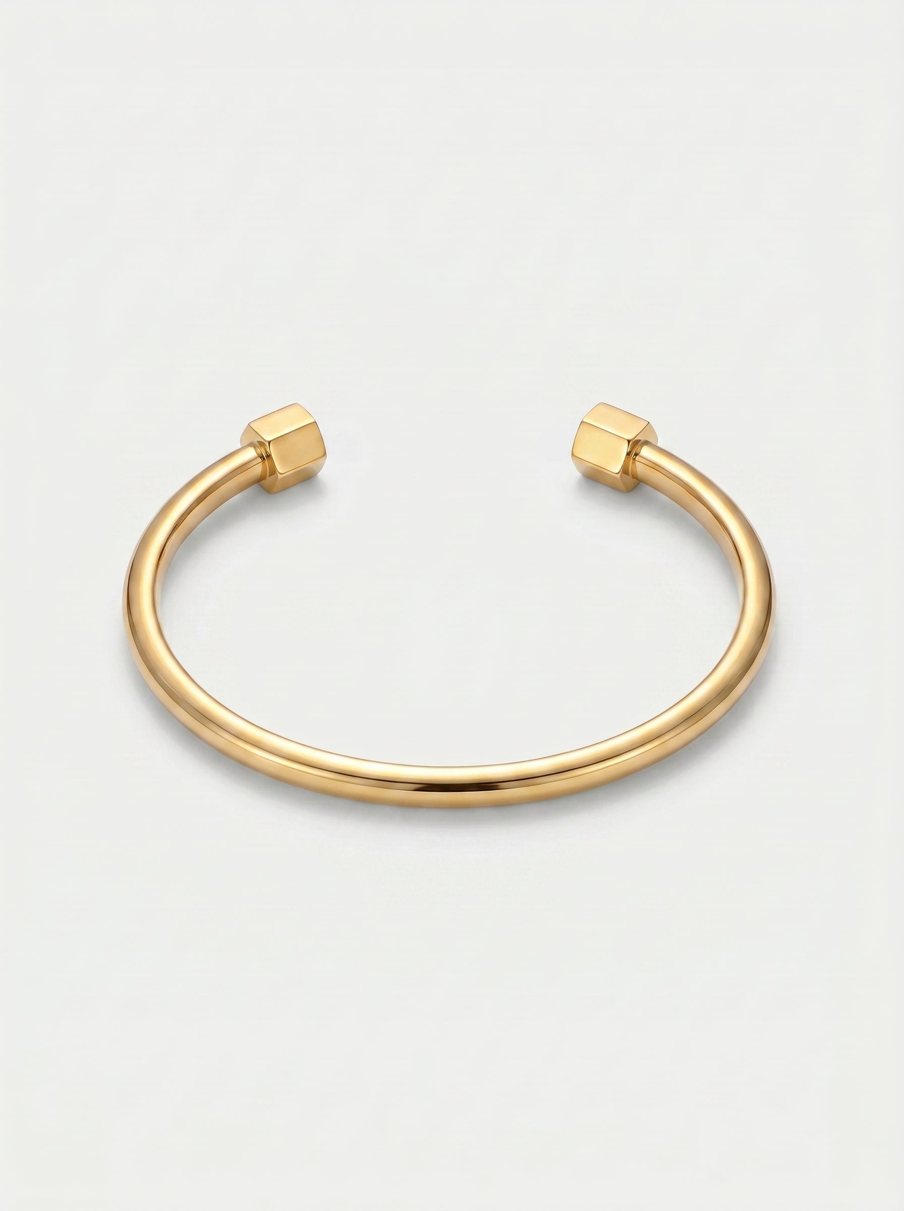 Pulseira dourada rígida com design aberto, acabamento polido e extremidades hexagonais, fotografada sobre fundo claro para um visual minimalista e moderno.