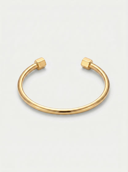 Pulseira dourada rígida com design aberto, acabamento polido e extremidades hexagonais, fotografada sobre fundo claro para um visual minimalista e moderno.