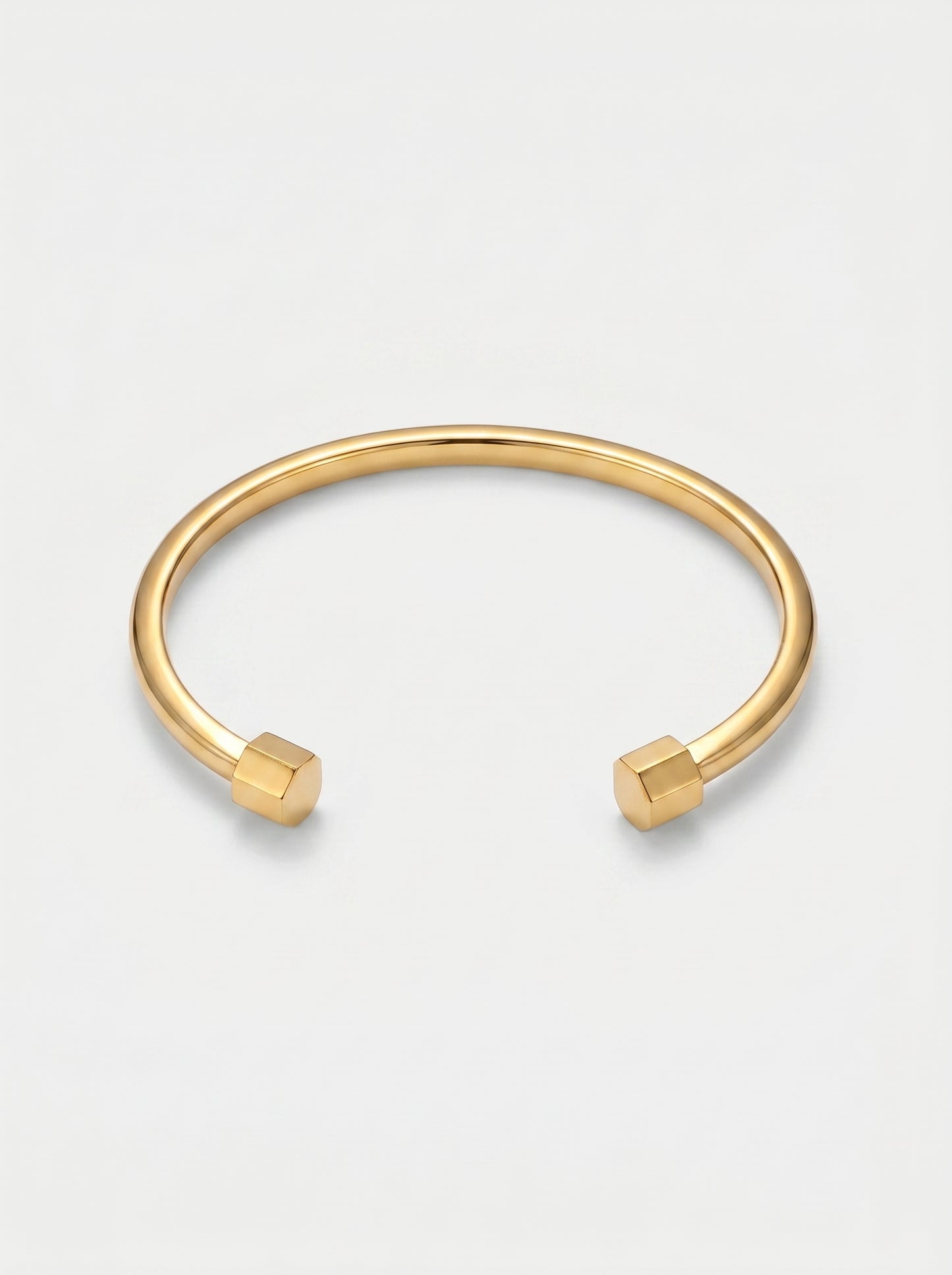 Pulseira dourada rígida com design aberto, acabamento polido e extremidades hexagonais, fotografada sobre fundo claro para um visual minimalista e moderno.