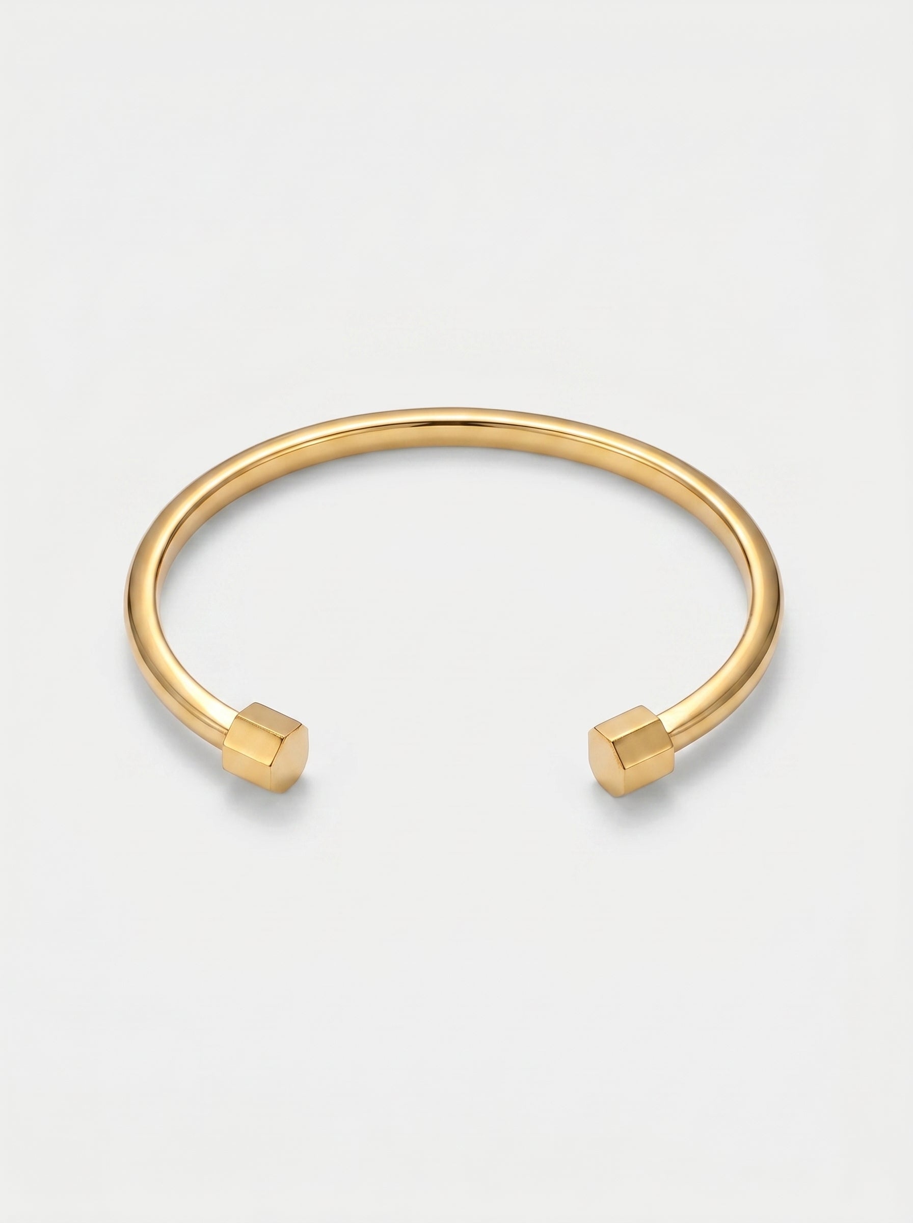 Pulseira dourada rígida com design aberto, acabamento polido e extremidades hexagonais, fotografada sobre fundo claro para um visual minimalista e moderno.