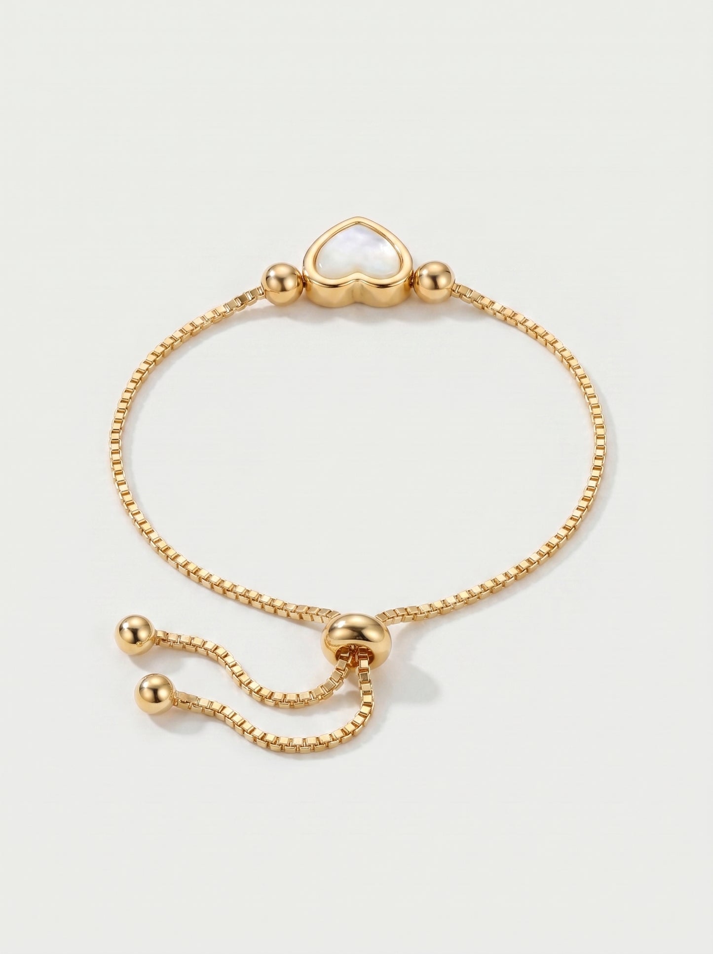 Pulseira dourada delicada com pendente em forma de coração branco, corrente ajustável e acabamento brilhante, fotografada sobre fundo claro para um visual elegante, feminino e romântico.