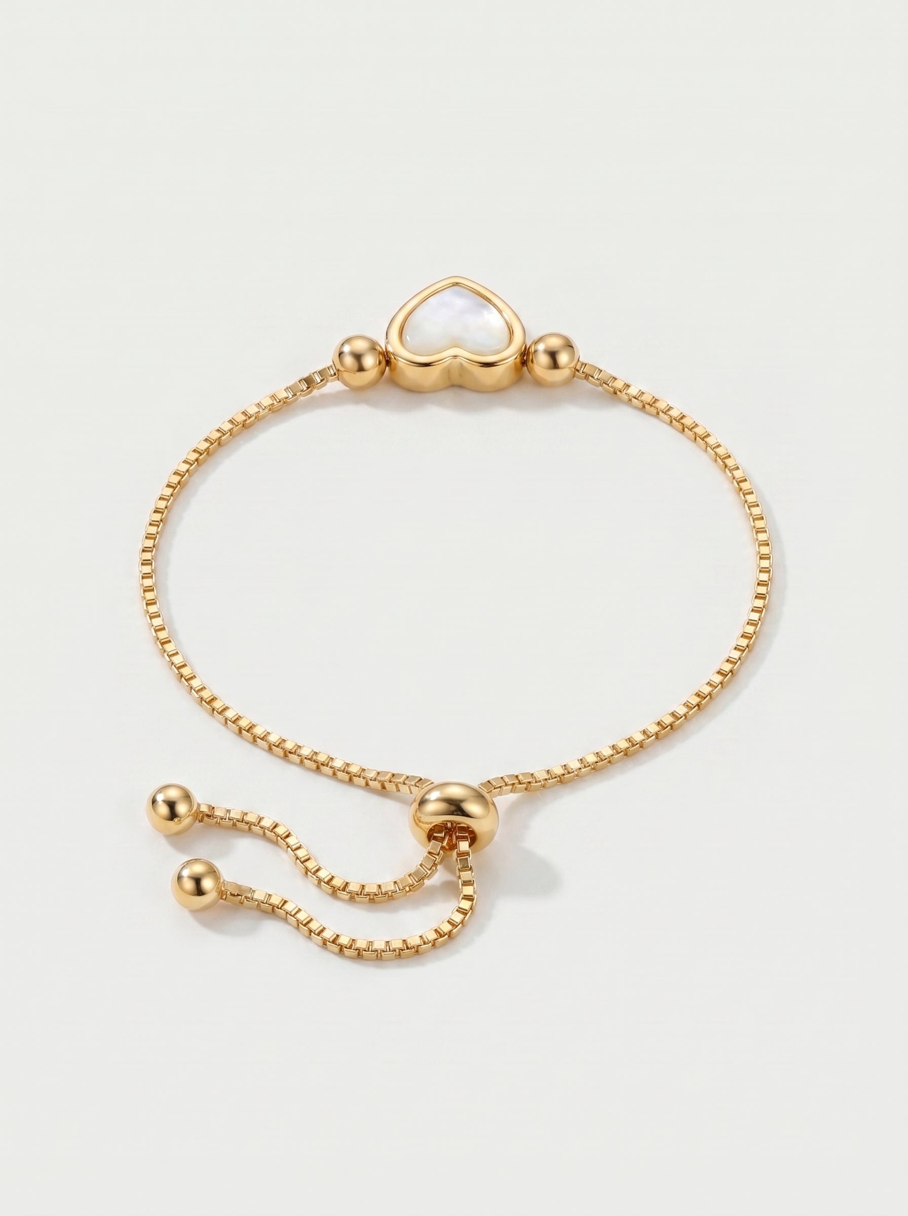 Pulseira dourada delicada com pendente em forma de coração branco, corrente ajustável e acabamento brilhante, fotografada sobre fundo claro para um visual elegante, feminino e romântico.