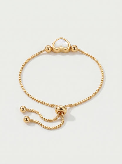 Pulseira dourada delicada com pendente em forma de coração branco, corrente ajustável e acabamento brilhante, fotografada sobre fundo claro para um visual elegante, feminino e romântico.