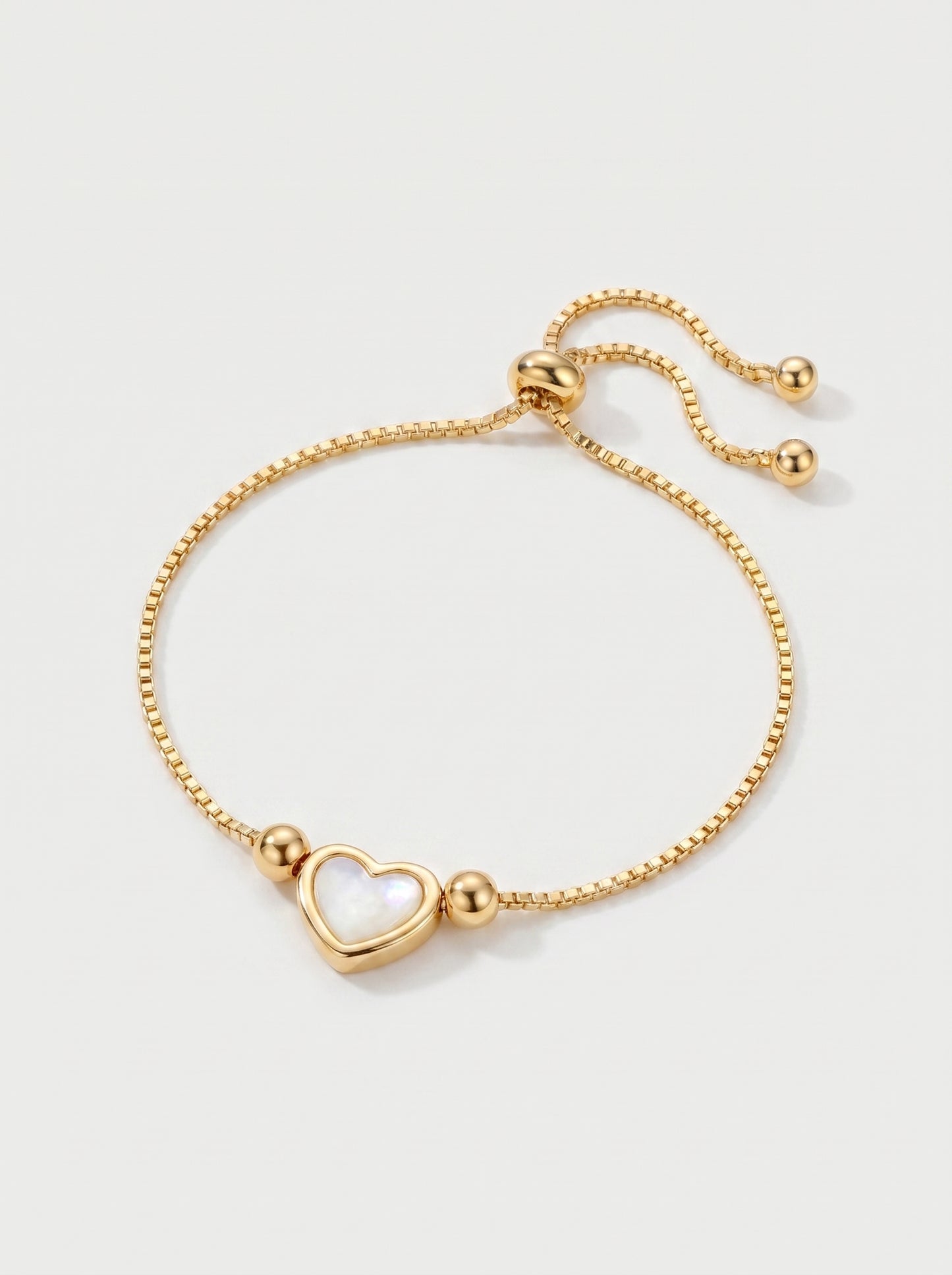 Pulseira dourada delicada com pendente em forma de coração branco, corrente ajustável e acabamento brilhante, fotografada sobre fundo claro para um visual elegante, feminino e romântico.