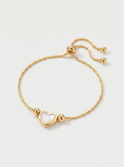 Pulseira dourada delicada com pendente em forma de coração branco, corrente ajustável e acabamento brilhante, fotografada sobre fundo claro para um visual elegante, feminino e romântico.