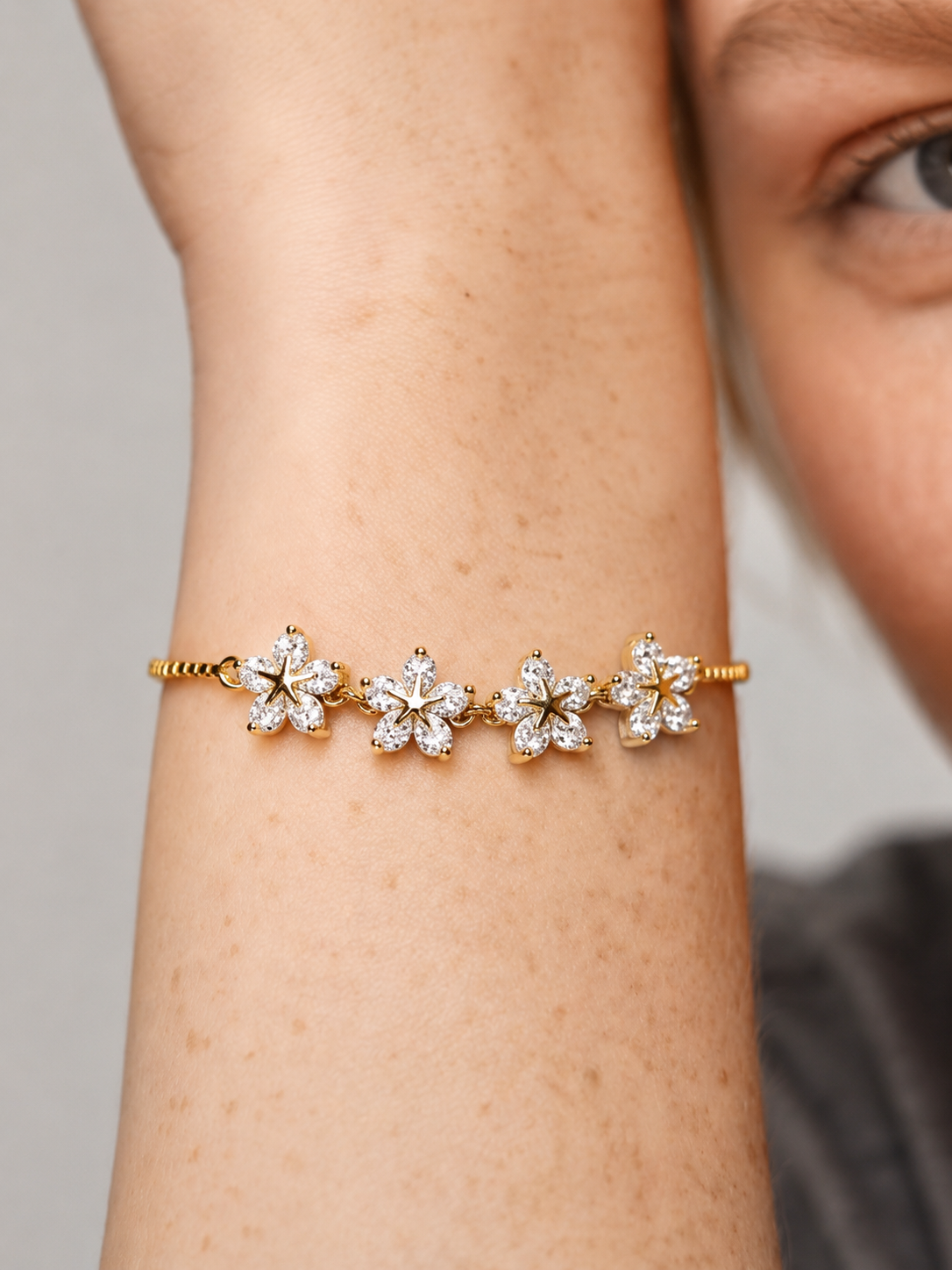 Pulseira dourada elegante com flores em cristais brilhantes e corrente fina, usada no pulso para um visual feminino, delicado e luminoso.