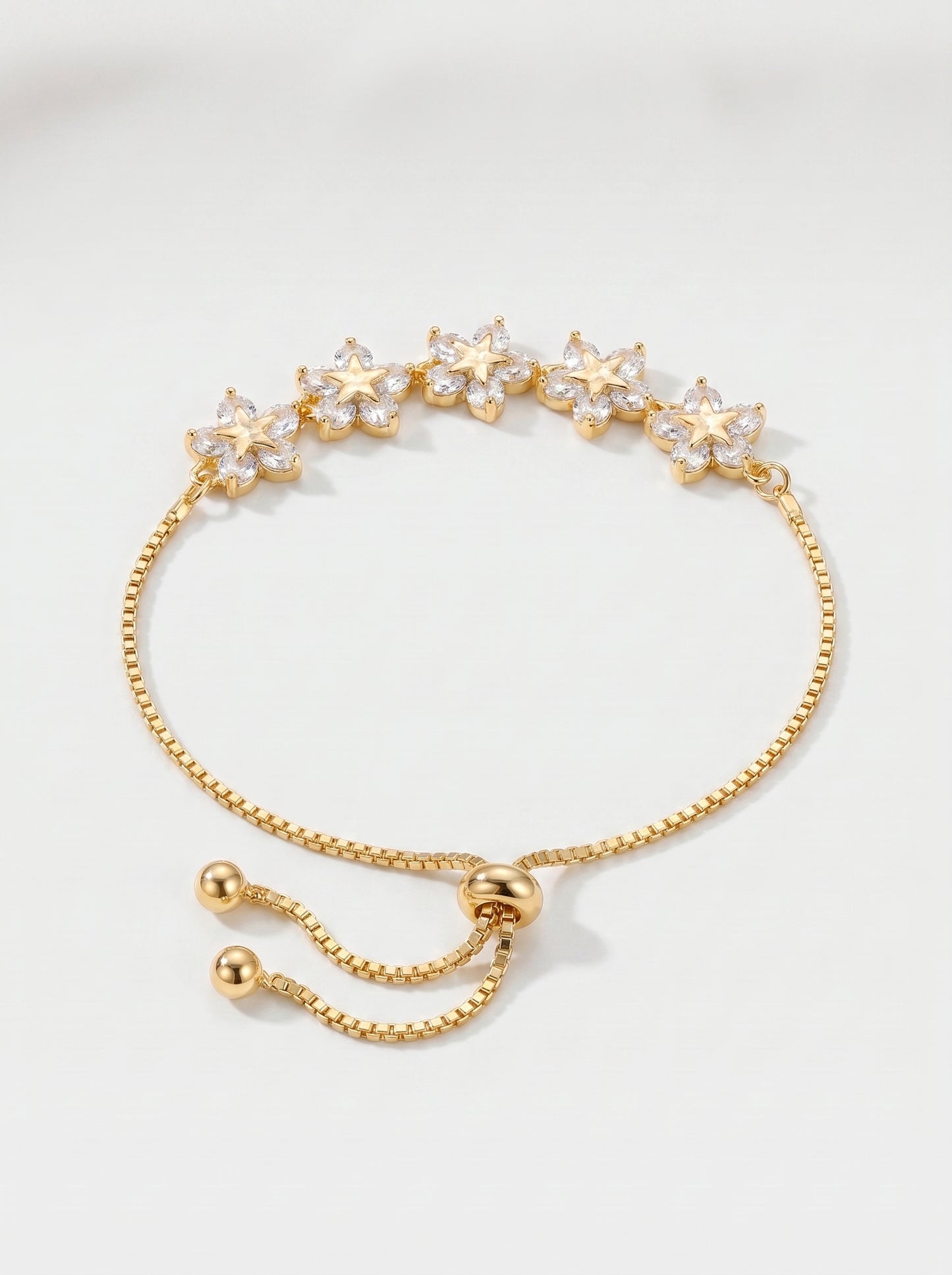 Pulseira dourada delicada com flores em cristais, corrente ajustável e acabamento brilhante, fotografada sobre fundo claro para um visual feminino, elegante e luminoso.
