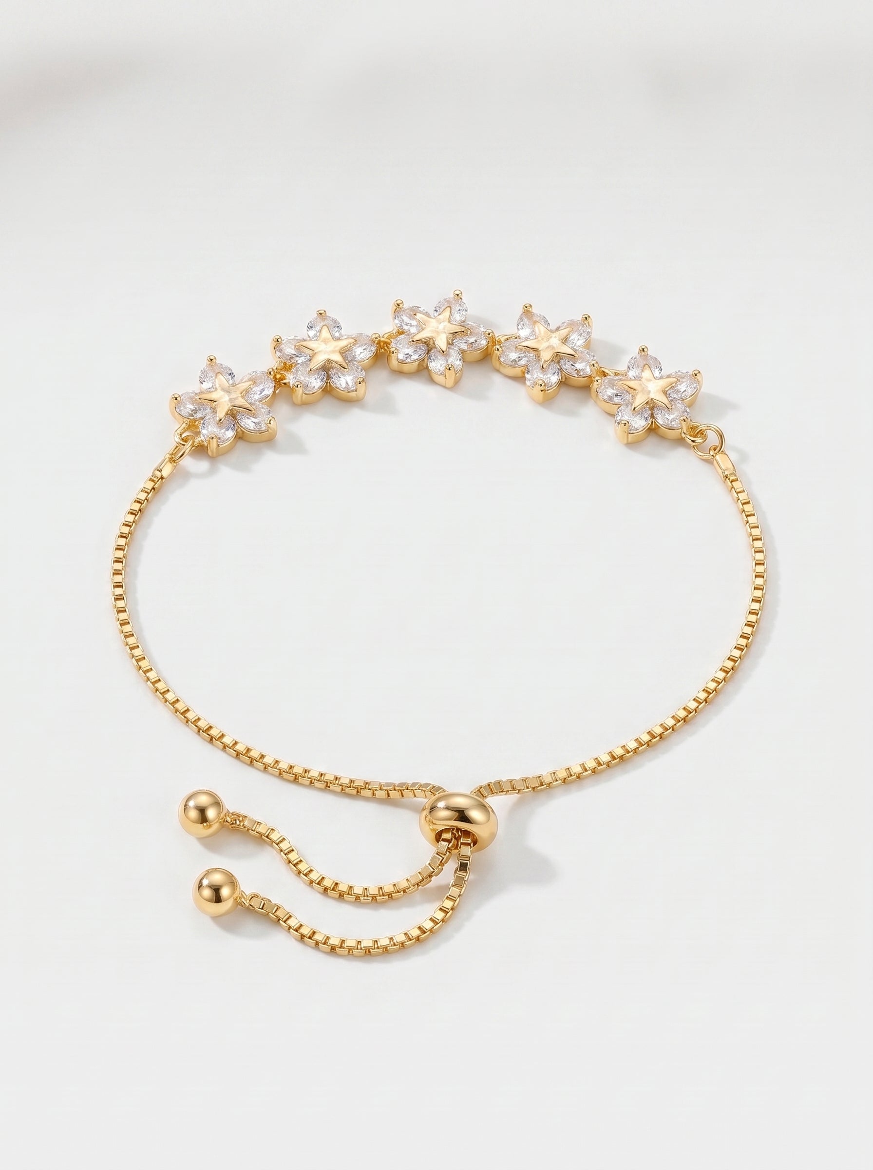 Pulseira dourada delicada com flores em cristais, corrente ajustável e acabamento brilhante, fotografada sobre fundo claro para um visual feminino, elegante e luminoso.