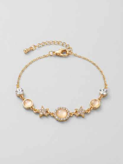 Pulseira dourada delicada com cristais brilhantes, detalhes em estrela e pendente circular central, fotografada sobre fundo cinzento claro para um visual elegante, feminino e sofisticado.