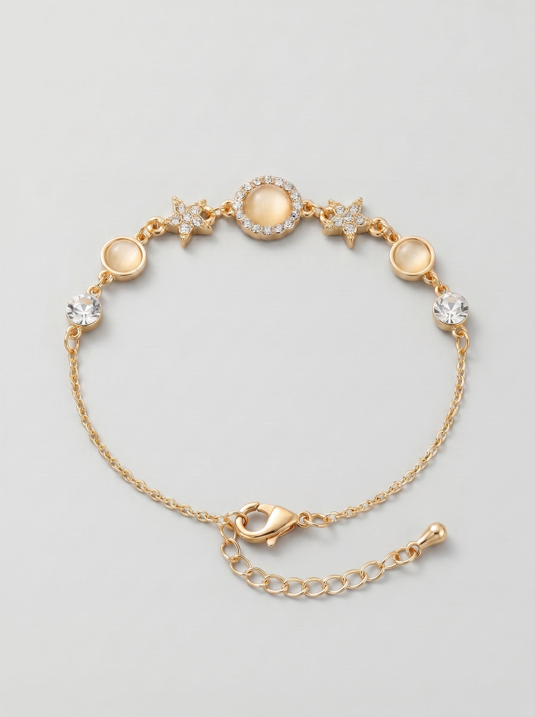 Pulseira dourada delicada com cristais brilhantes, detalhes em estrela e pendente circular central, fotografada sobre fundo cinzento claro para um visual elegante, feminino e sofisticado.
