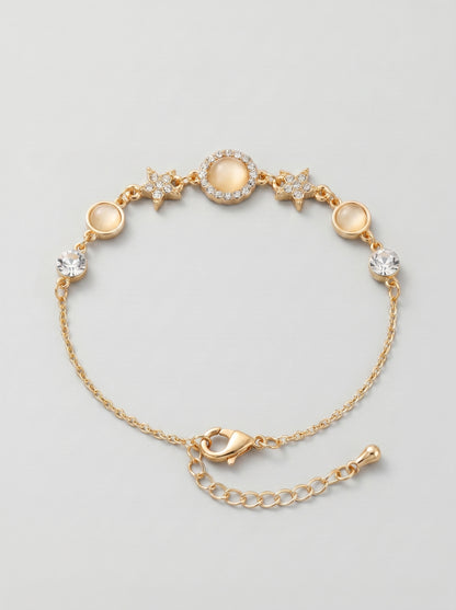 Pulseira dourada delicada com cristais brilhantes, detalhes em estrela e pendente circular central, fotografada sobre fundo cinzento claro para um visual elegante, feminino e sofisticado.