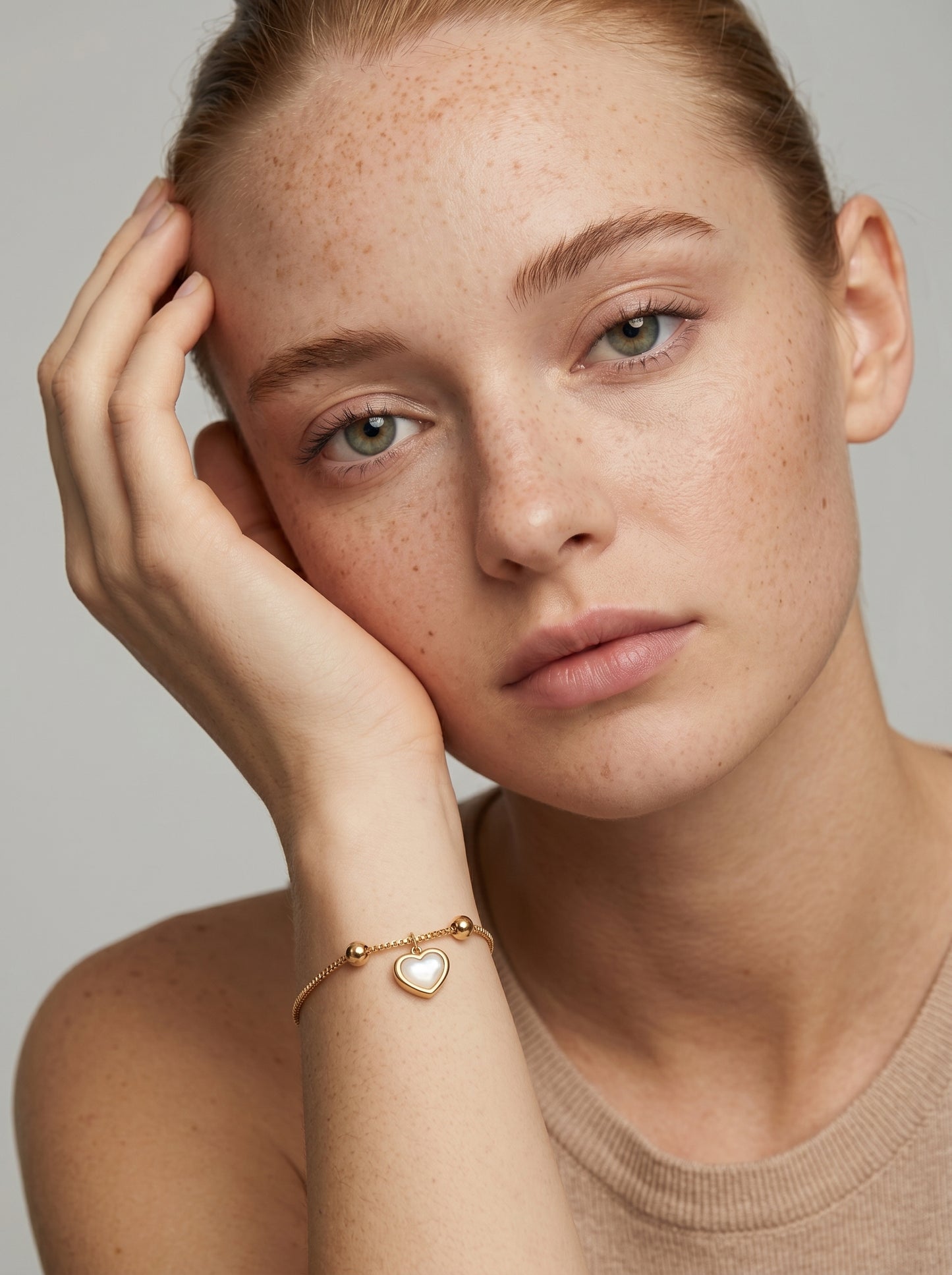 Pulseira dourada delicada com pendente em forma de coração branco e acabamento brilhante, usada por uma modelo para um visual elegante, feminino e romântico.