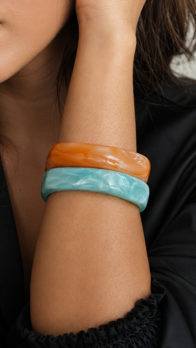 Pulseiras de resina em azul turquesa e laranja usadas no pulso, com acabamento brilhante e estilo elegante.