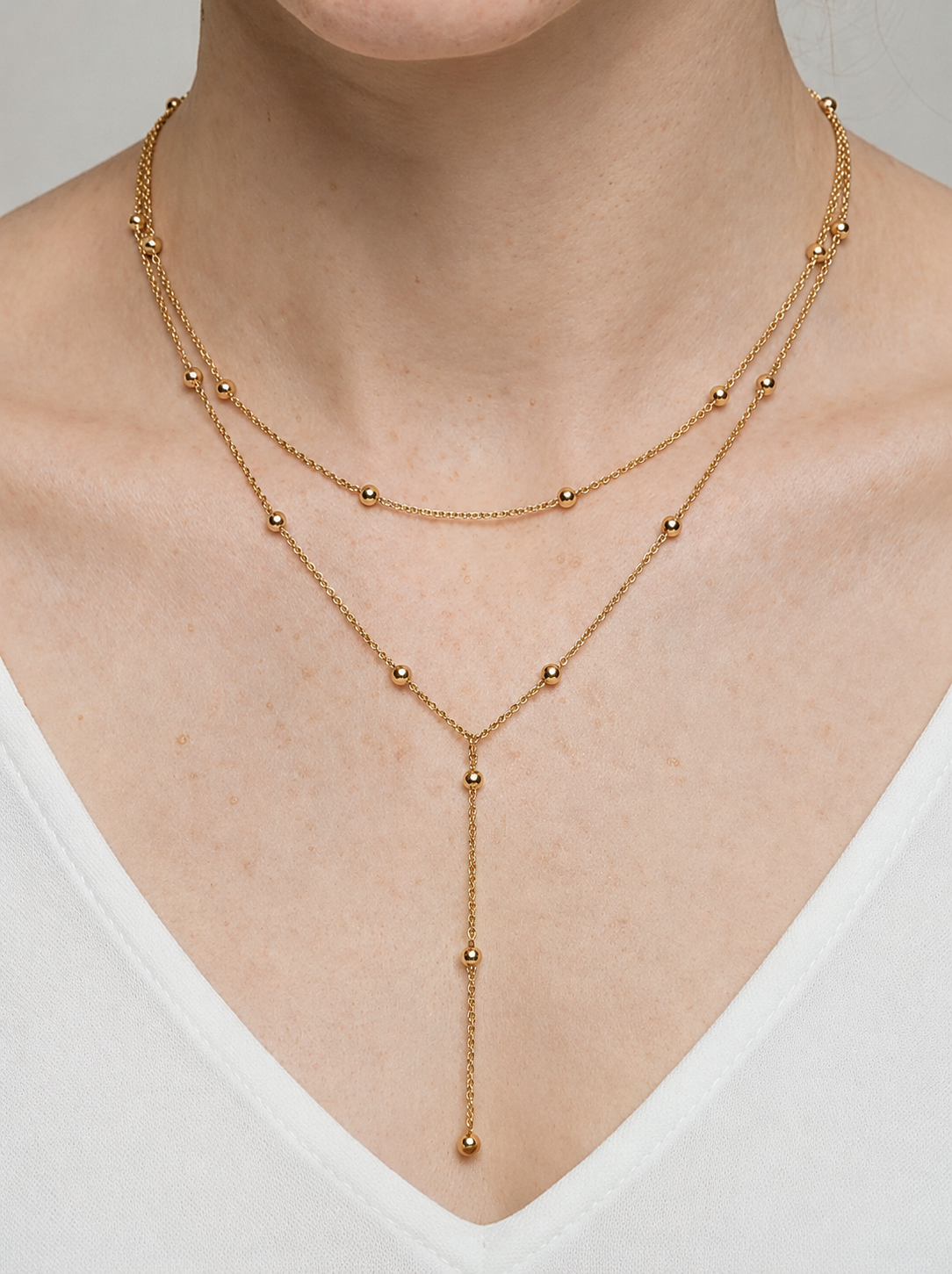 Colar dourado comprido em camadas com detalhes em esferas e pendente delicado, usado ao pescoço para um visual elegante, sofisticado e moderno.
